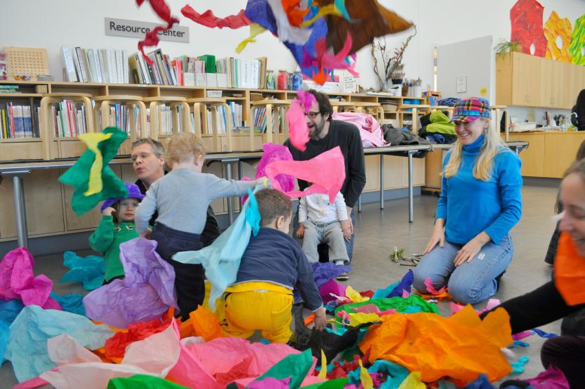 Children tearing down a tissue paper mountain as adults watch, smiling. 