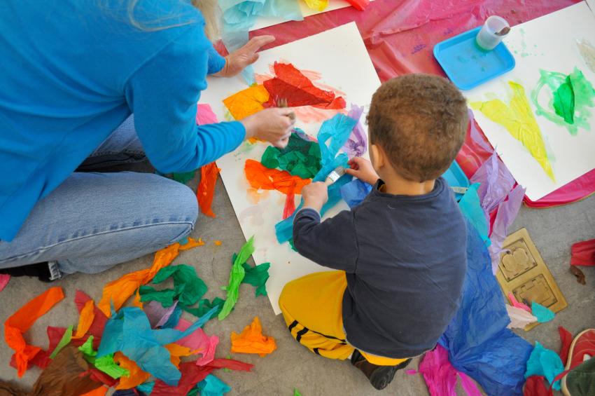 A child gluing tissue paper onto a large watercolor paper. 