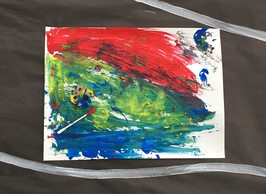 Abstract painting on a wall display with blue, red, and green paint and a cotton swab and cardboard stamp attached.