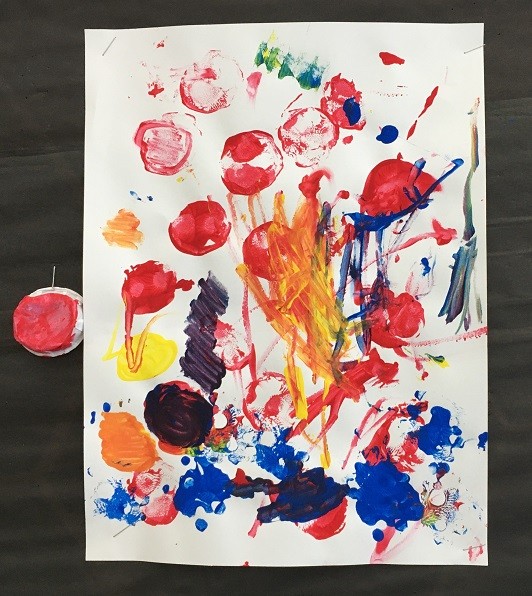Painting with stamped red circles, stamped blue cardboard pieces, and energetic orange brushstrokes. The cup used to stamp in red is stapled to the wall next to the artwork.