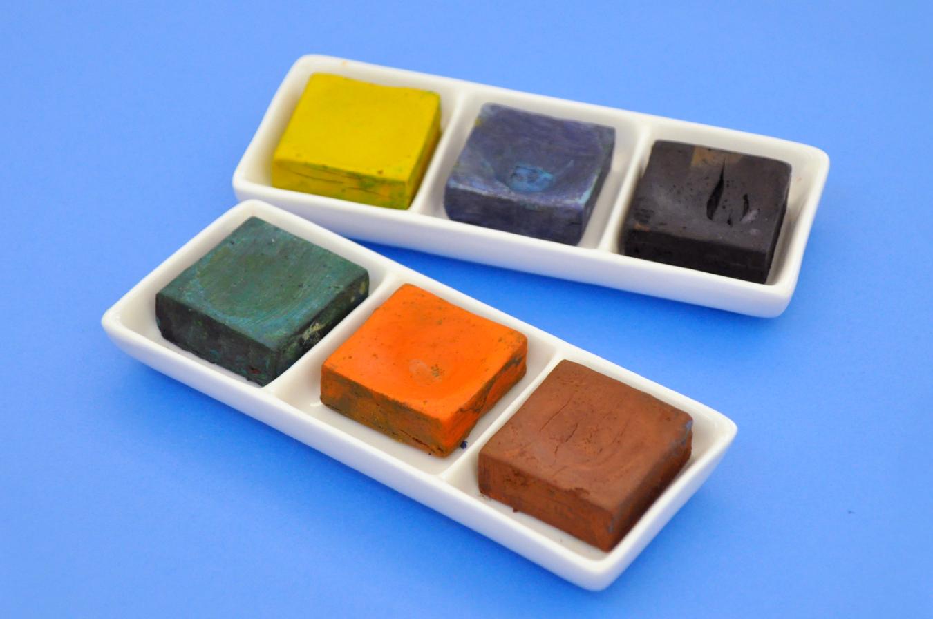 Two sets of dried tempera paint cakes with three colors in each set.