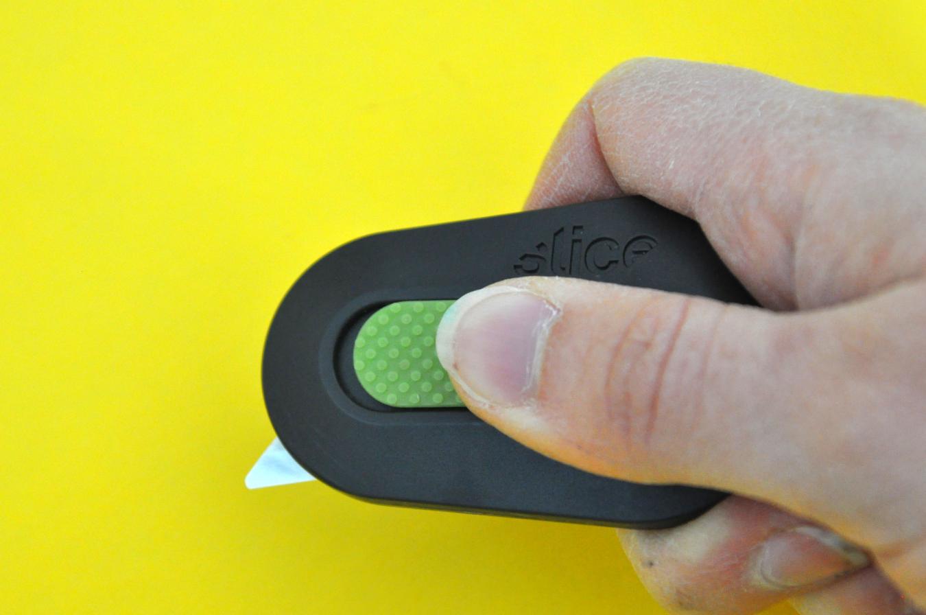 A hand slides a ceramic box cutter blade out from a plastic holder.
