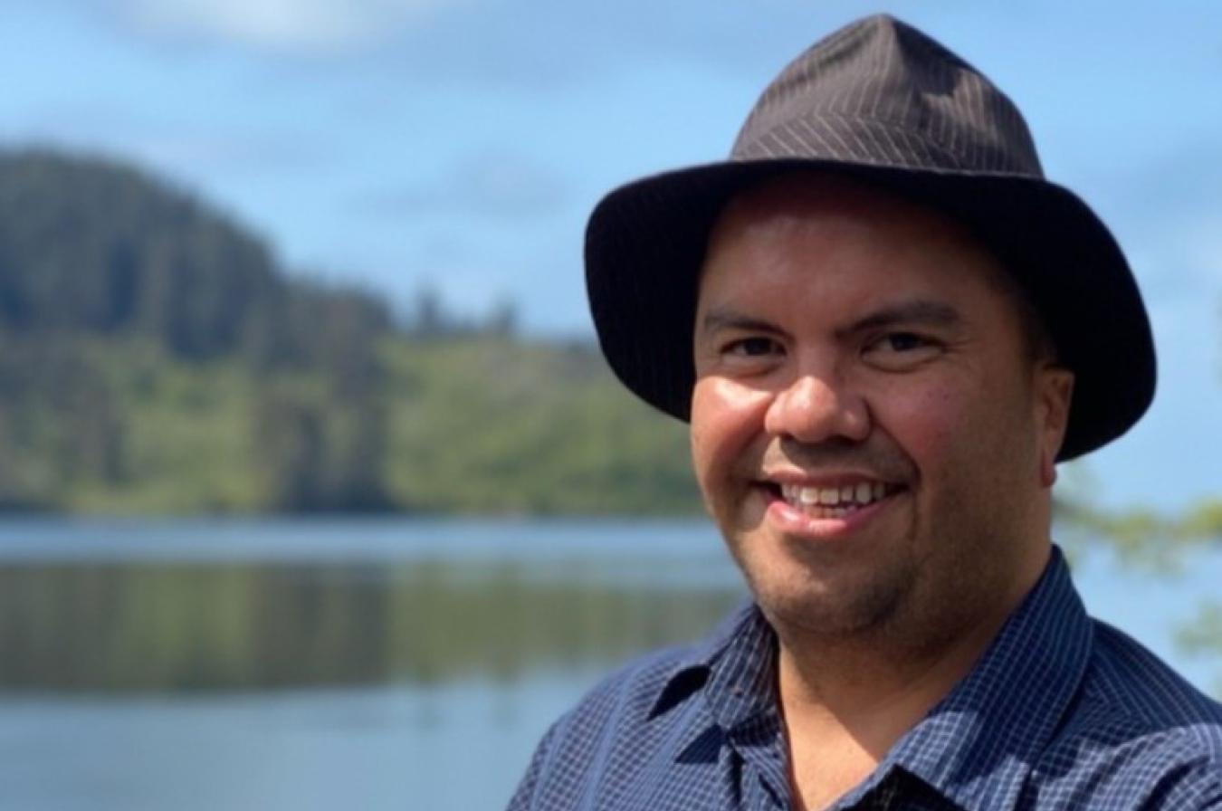 man in a blue shirt and black hat with lake and trees in the background