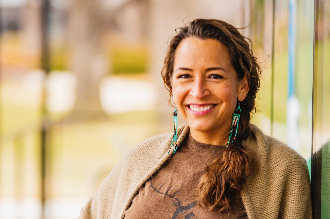 woman smiling with blue beaded earrings and brown hair with a brown top