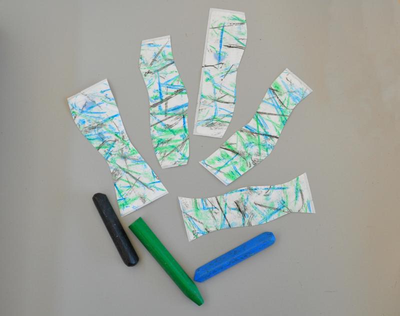 Black, green, and blue crayons next to a fan of colorful sticker strips.