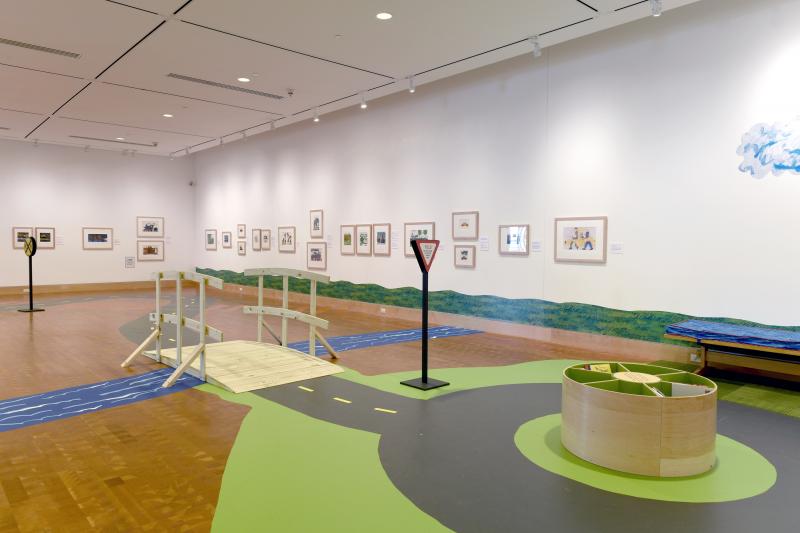 Installation image showing walls with framed art and bridge to reading area.