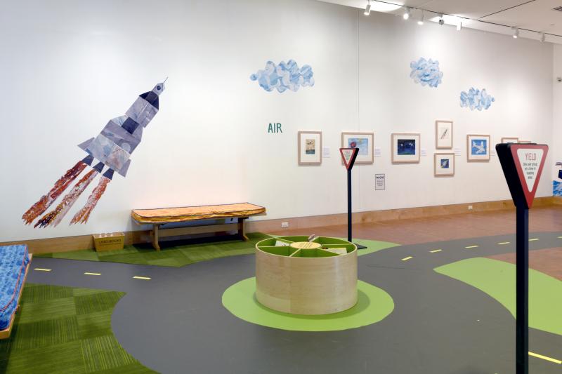 Installation image showing walls with framed art and reading are with large rocket graphic.