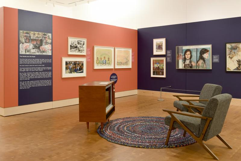 Installation image showing walls with framed art and video viewing area.