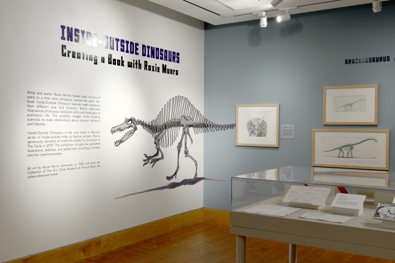 Installation image showing introduction wall with art and dinosaur skeleton mural.
