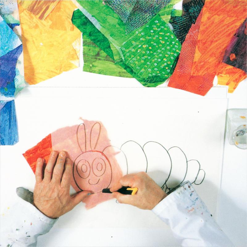 hands with a utility blade cutting out the pencil drawing of the caterpillar with a piece of red tissue paper visible under the tracing paper