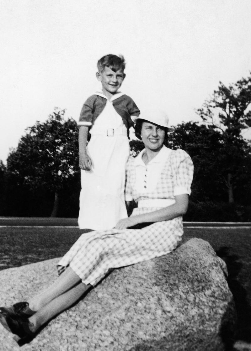 black and white photograph of woman sitting on a rock, with boy standing next to her