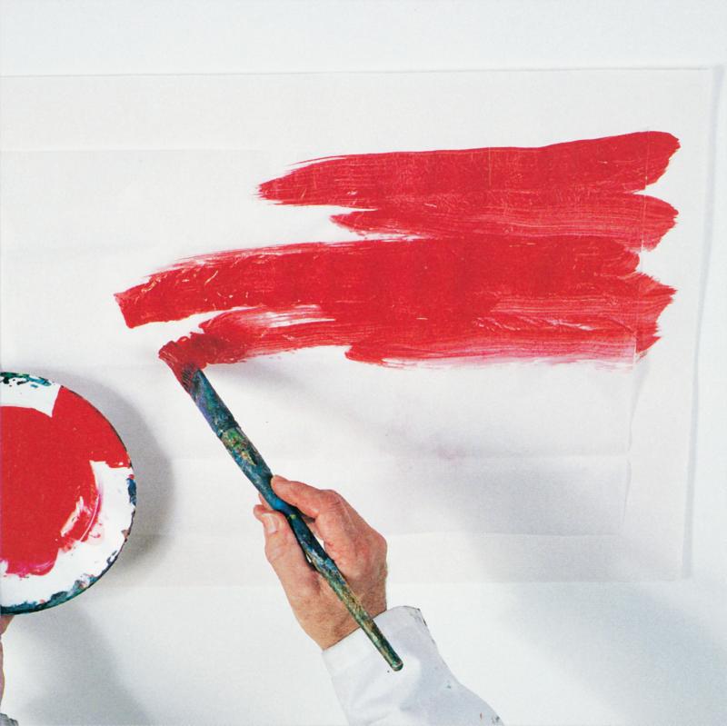 hand with paintbrush adding read paint to a white piece of tissue paper