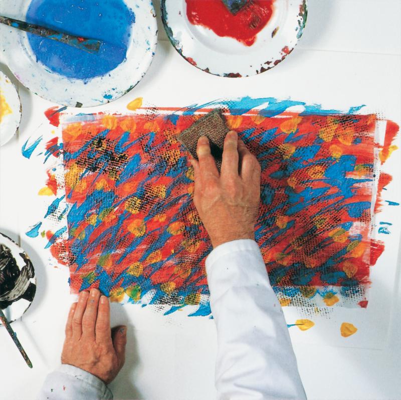hand holding carpet square and pressing it down on painted tissue paper