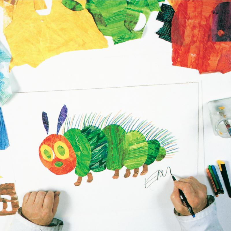 Completed red, green, yellow, and blue caterpillar collage with hand holding a pen and signing the word Eric under the caterpillar