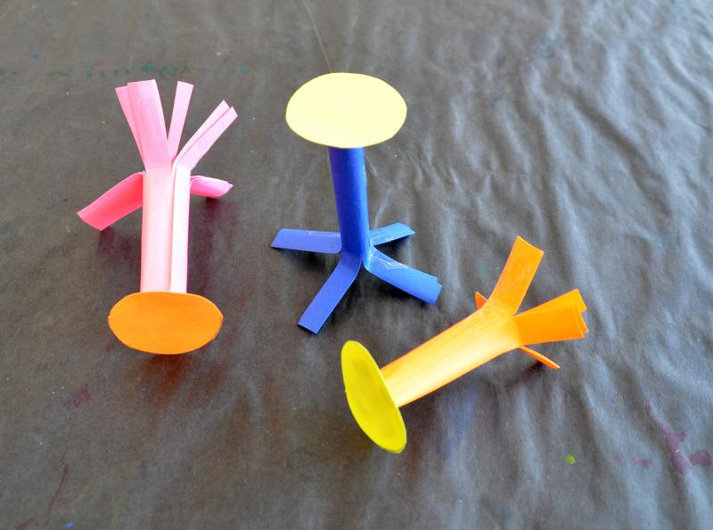 three paper pegs made by attaching colorful discs to rolled-paper cylinders.