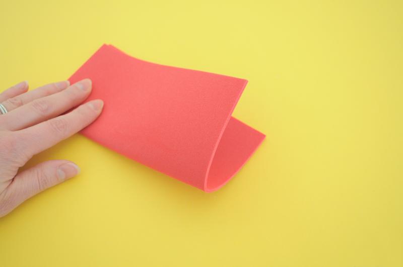 A hand folds a pink piece of thin foam in half.