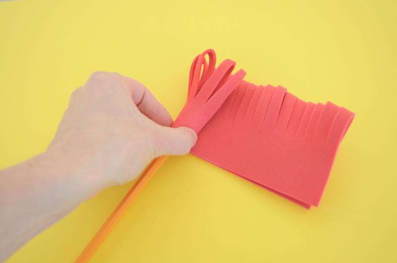A hand rolls the cut foam around the end of a pencil.