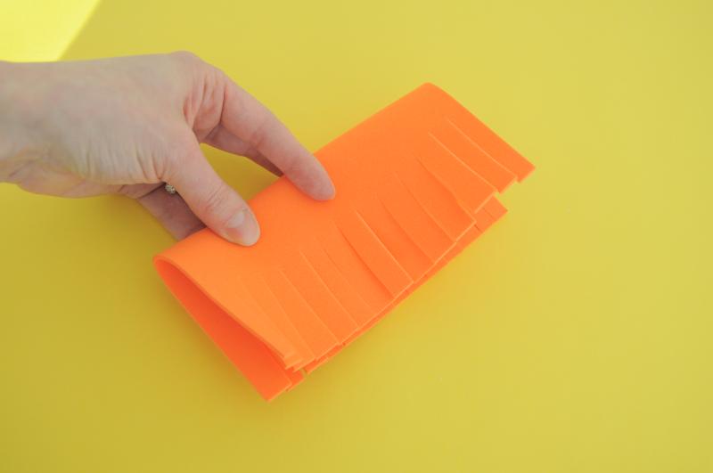 A hand folding a thin piece of orange foam in half, with cuts made on the open edges.