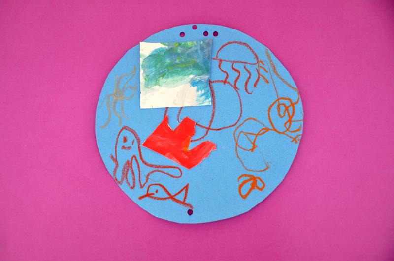 An ocean scene with many sea creatures made with red and orange oil pastels and collage papers.