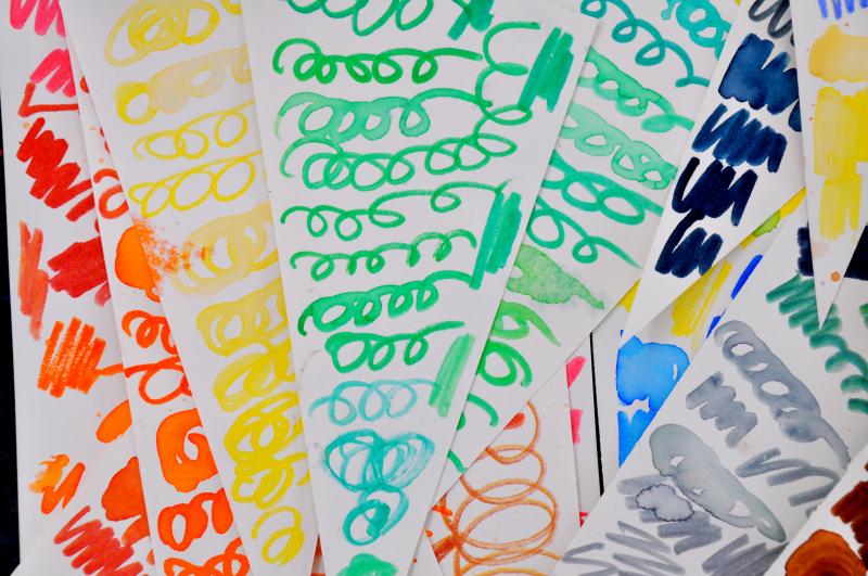 A stack of colorful papers with various colorful marks on them made during the marker-reviving process.