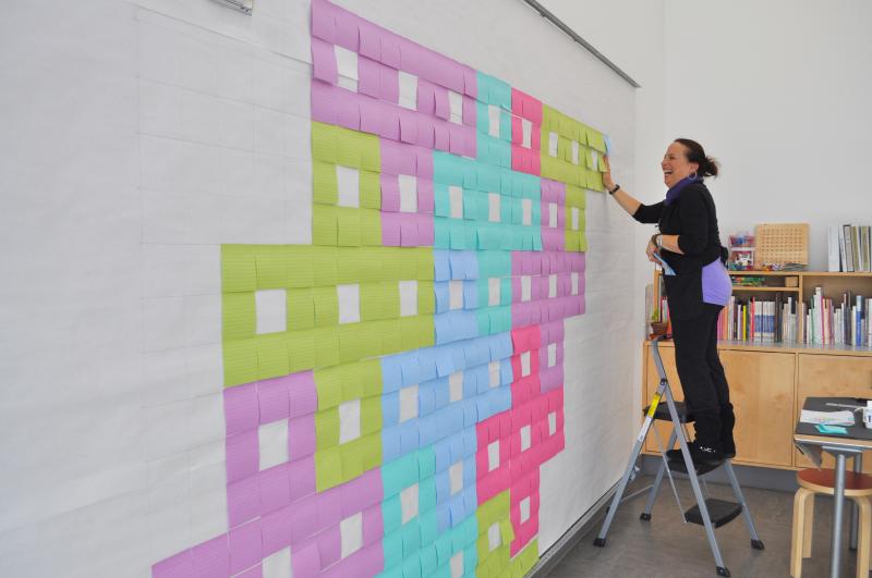 A volunteer installing Post-Its onto the display wall.