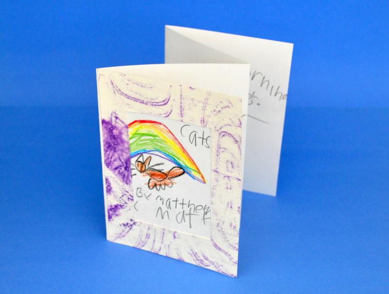 The cover of an accordion fold book with a cut-out frame and drawings of a cat and a rainbow.