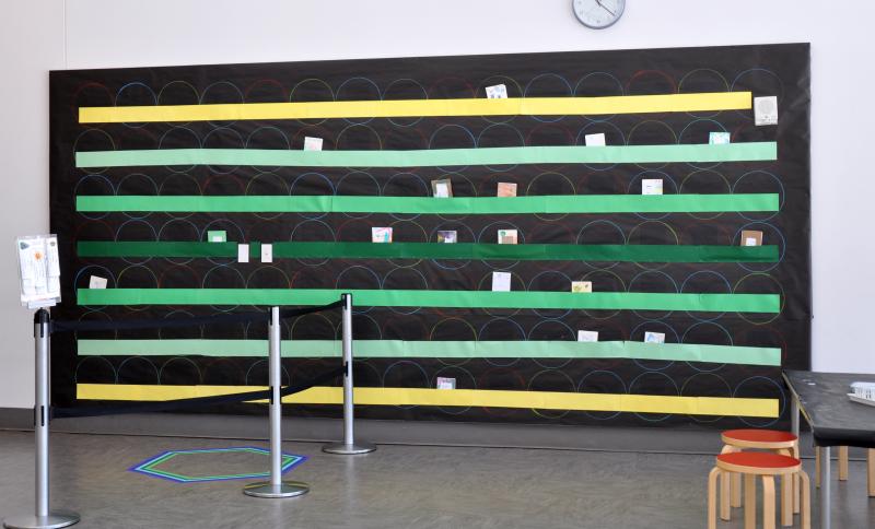 Art Studio bulletin board with black background paper and horizontal construction paper stripes in different shades of green and yellow.