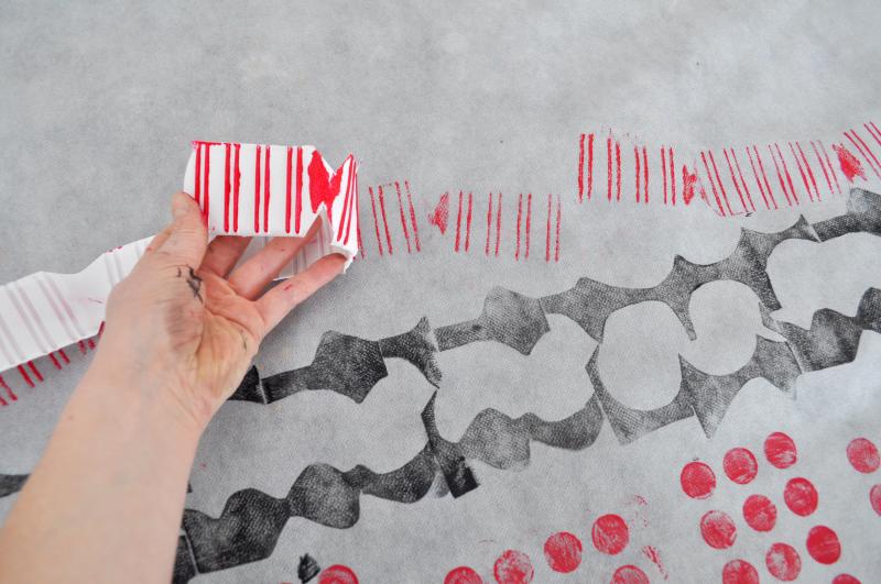 A hand pulls back a long strip of plastic to reveal a red print on white paper.