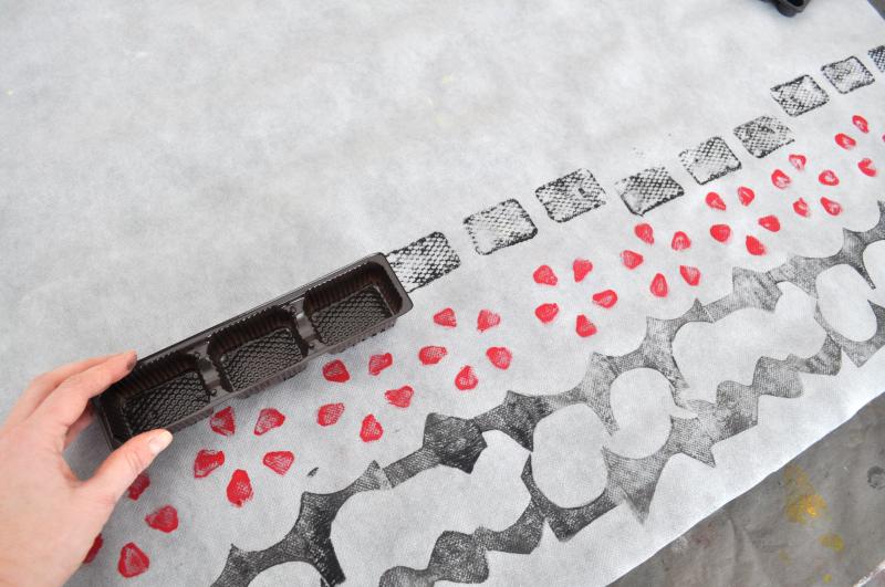 A hand presses a plastic box onto a white paper, making a black rectangle stamp.