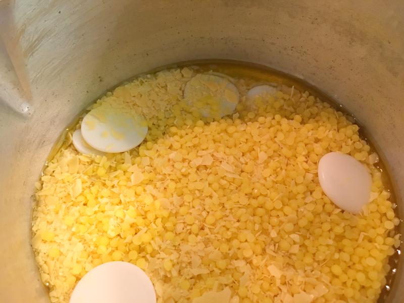 Wax pellets and cocoa butter coins in a pot slowly melting around the edges.