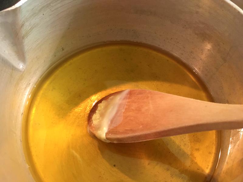Melted wax in a pot being stirred by a wooden spoon.