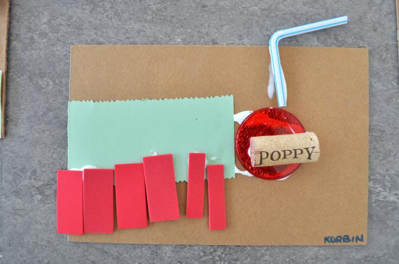 A mixed-media collage of a caterpillar created from paper, plastic caps, straws, and corks.