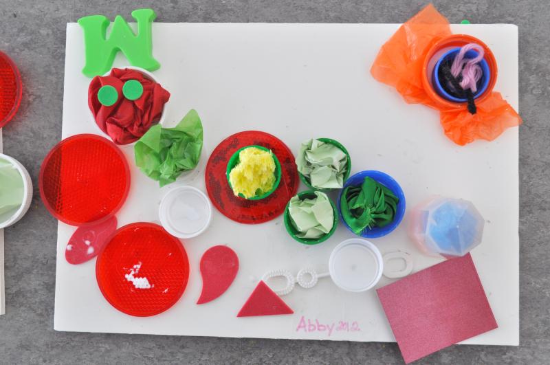 A caterpillar mixed-media collage where the body segments are made from bottle caps filled with crumpled tissue paper.