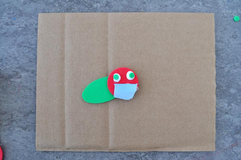 A small caterpillar mixed-media collage on a large piece of cardboard.