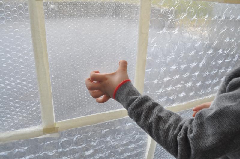 A young guest uses their thumb to pop bubble wrap on the window.