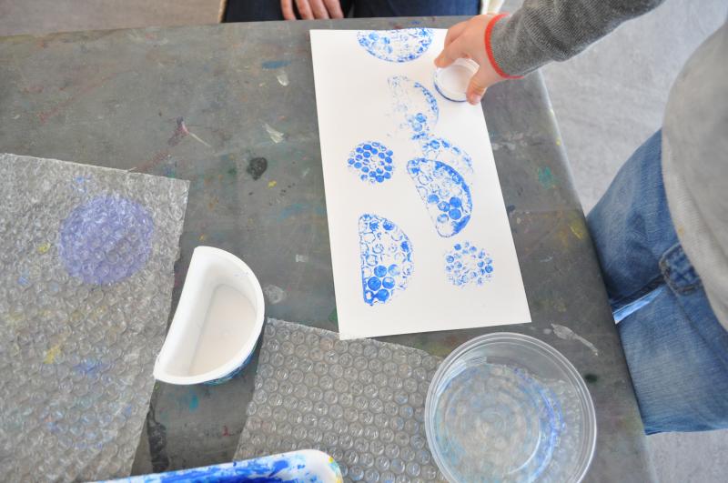 A young guest stamps with a bubble wrap stamp and blue paint onto a piece of paper.