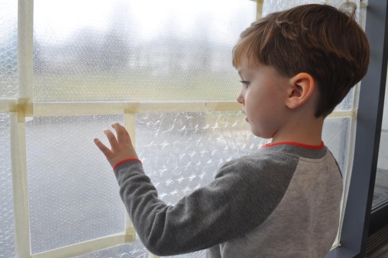 A young guest smiles while gently popping bubble wrap on the window.