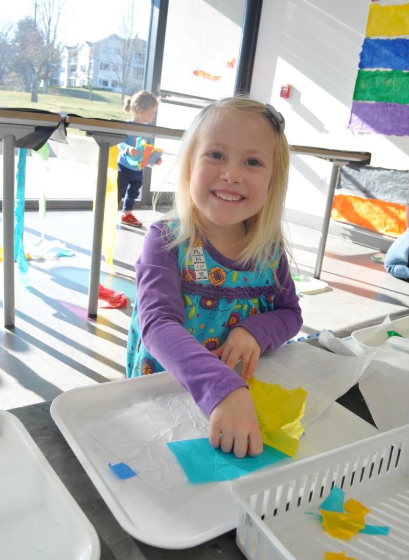 A young guest grins while placing their tissue paper onto contact paper.