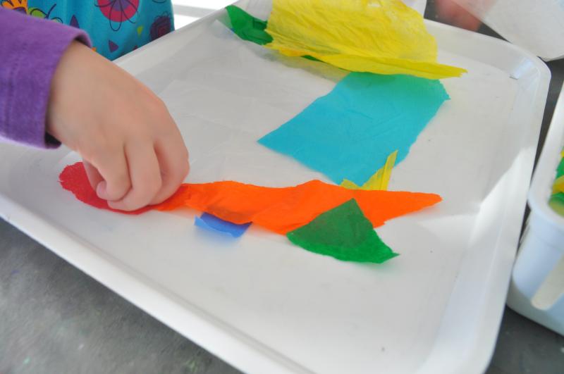 A young guest places colorful tissue paper onto a piece of sticky contact paper.