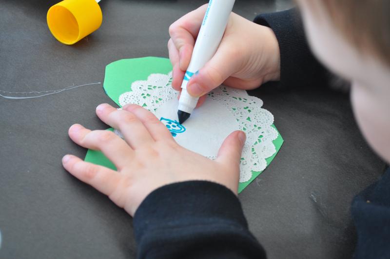 A child draws a smiling face onto a paper doily.