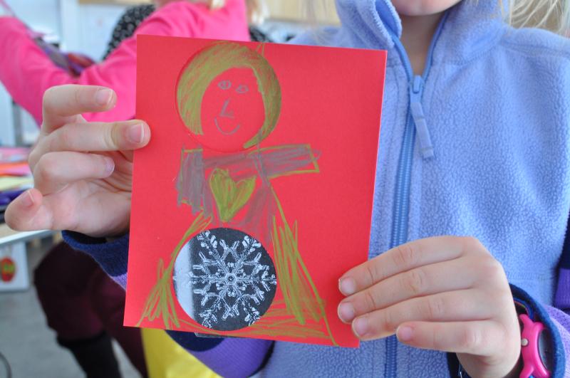 A child holds up a valentine card with a drawing of a person and a collaged snowflake.
