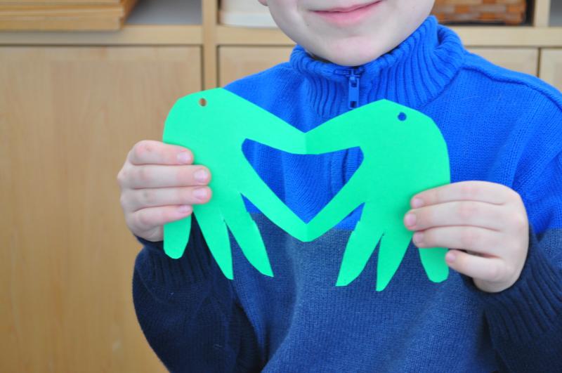 A child unfolds a valentine card that looks like two hands together, connected at the thumbs and pointer fingers to create the negative space of a heart.