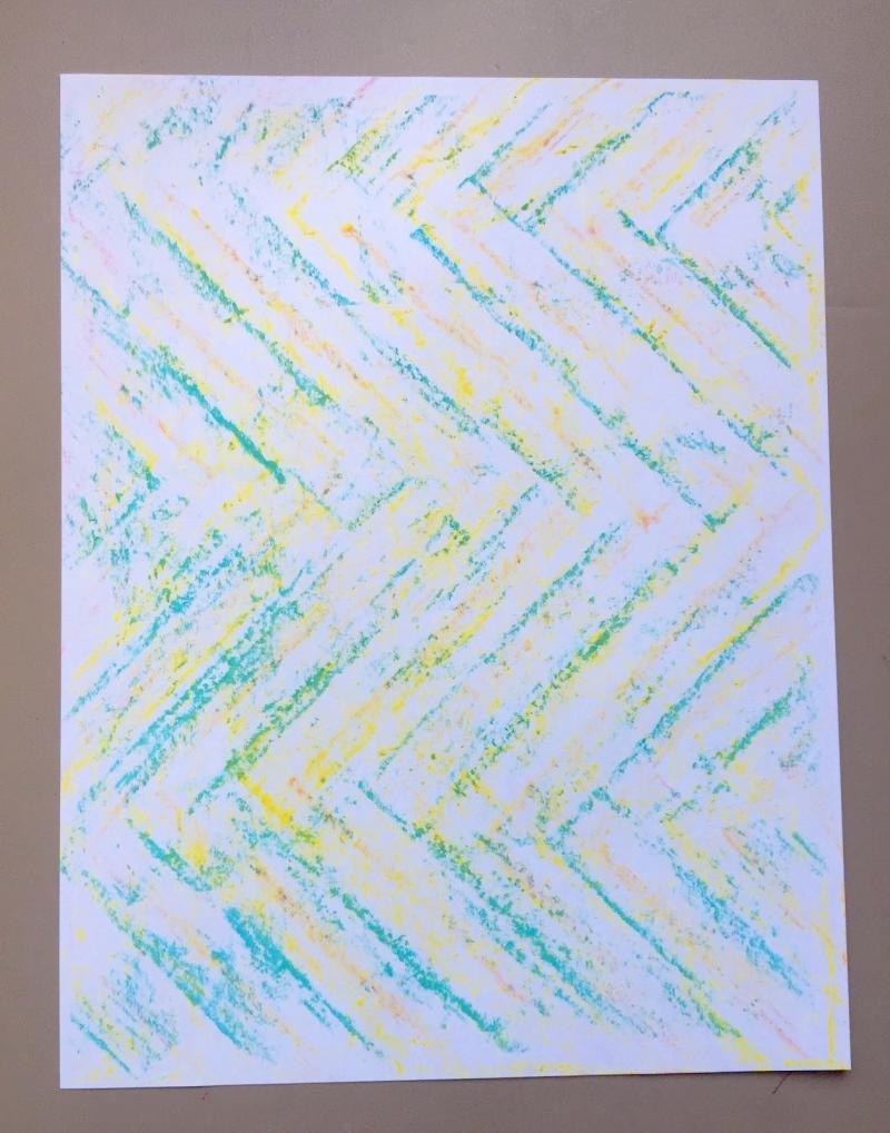 Multi-colored rubbings of large chevrons creating a pattern across a sheet of paper.