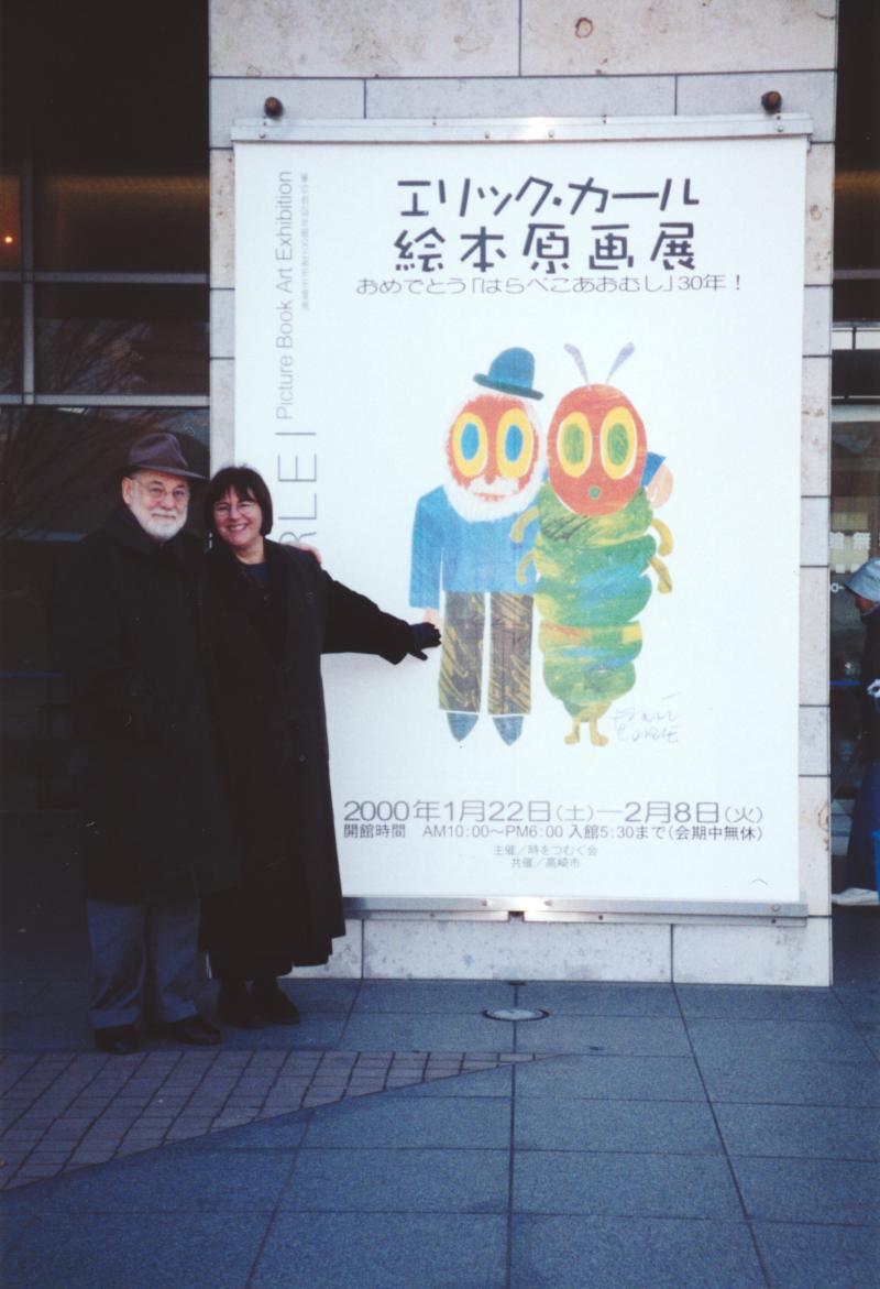 Photo of Eric and Barbara Carle in front of Very Hungry Caterpillar exhibition poster.