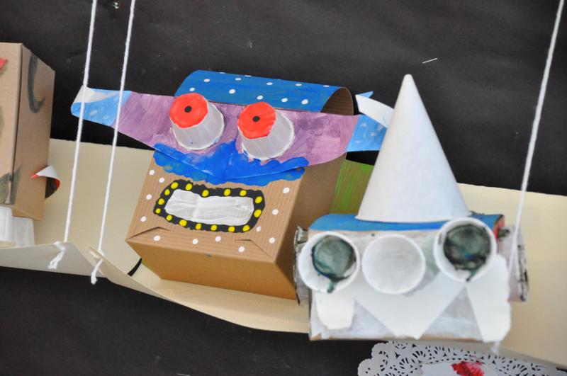 Two sculptures sitting on a shelf, one with dots of color, and bright red eyes made from cups.