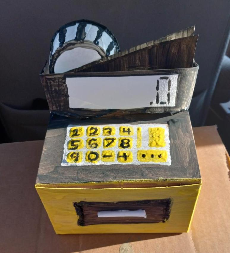 A cash register with yellow buttons made from a cardboard box.
