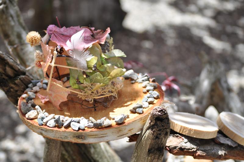 A handmade fairy house perched on a wooden tree trunk slice wedged within tree branches.