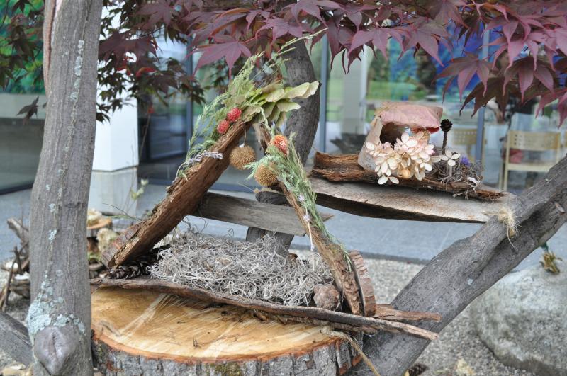 Two fairy houses made out of barks and grasses perched in trees on wooden planks and trunk slices.