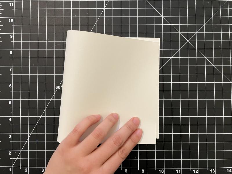 plain 6x12 inch paper folded in half to a square that is 6x6 inches, hand in photo motioning the fold