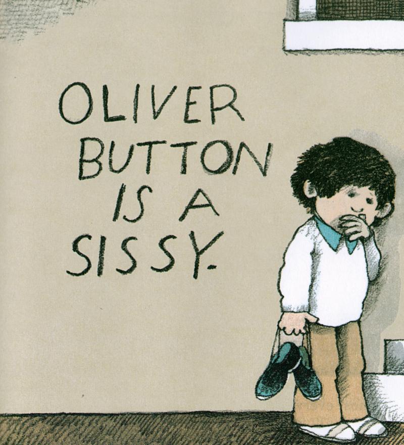 A child stand against a tan wall holding a pair of black shoes. On the wall are the words, &quot;Oliver Button Is A Sissy.&quot;